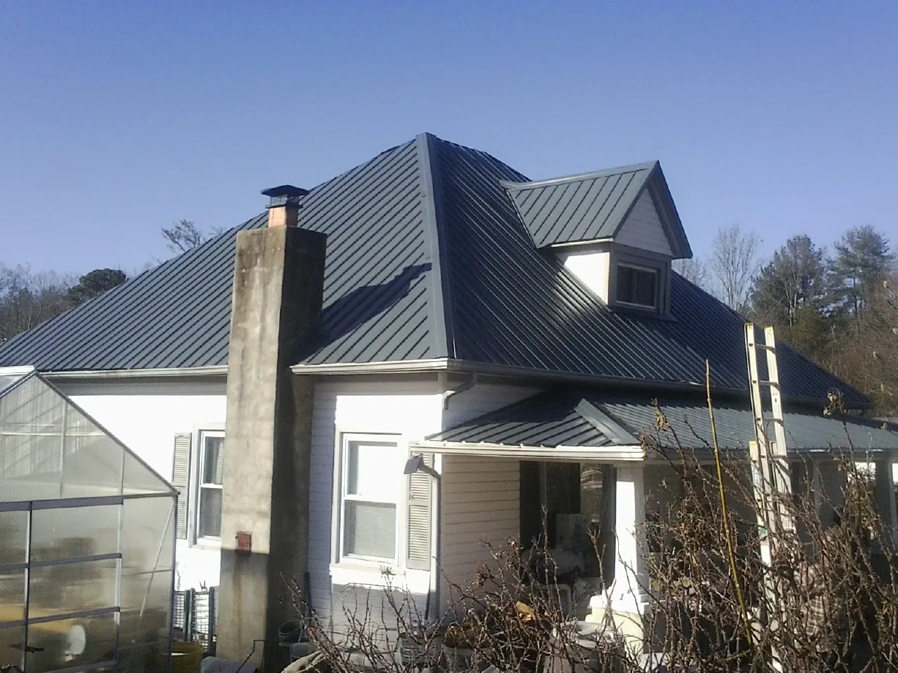 Dark blue standing seam metal roof on a white farmhouse with dormer — Slate & Tile Roof Repair by Roofing Brothers in Four Lakes