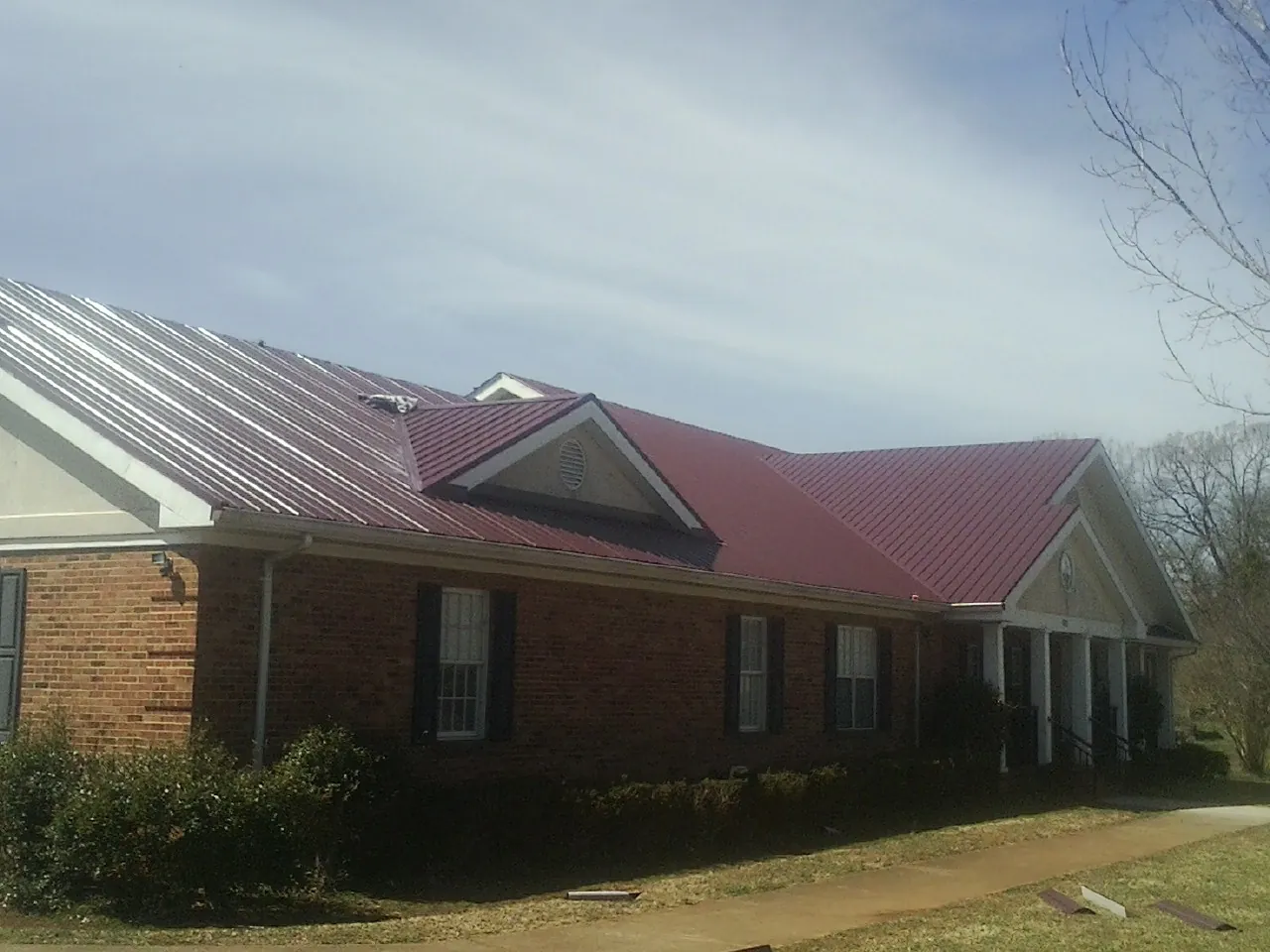 Red metal roof with gabled entries on a long brick building, from a Hail Damage Roof Repair job in Four Lakes