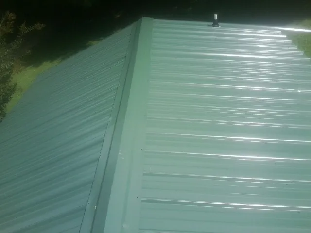 New green metal panels meeting at the ridge of a roof — Flat Roof Repair work by our crew in Four Lakes