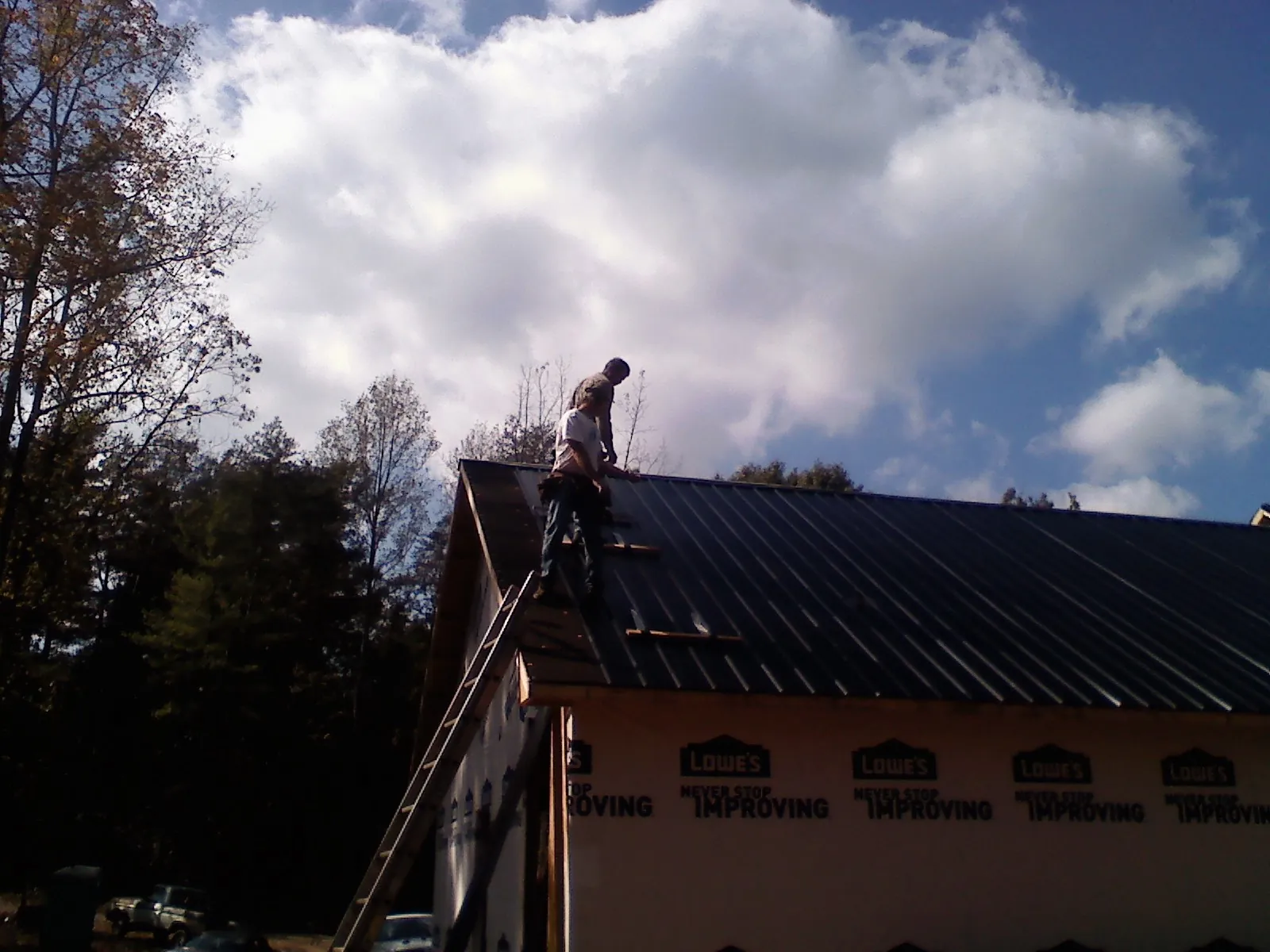 Roofer fastening dark metal panels high against a cloudy sky, from a Roof Inspection job in Four Lakes
