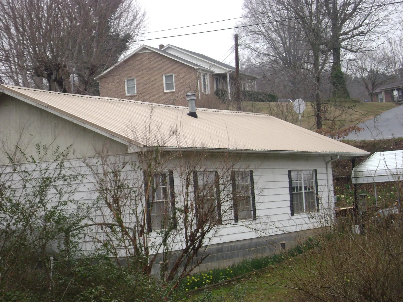 Tan metal roof on a white sided house set into a hillside — Commercial Roofing by Roofing Brothers in Four Lakes