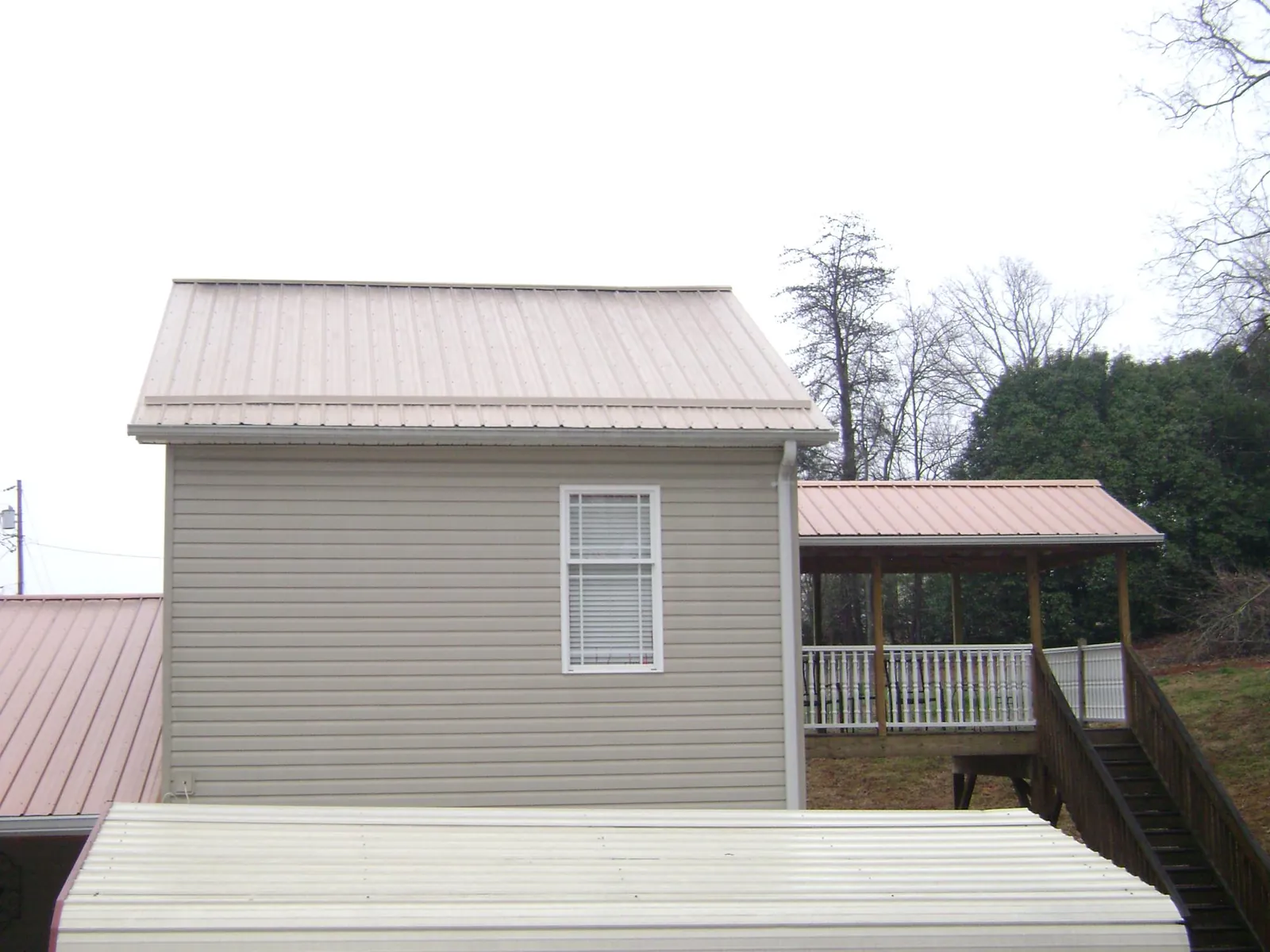 Tan metal roofs on a two story addition and attached porch, from a Roof Replacement job in Four Lakes